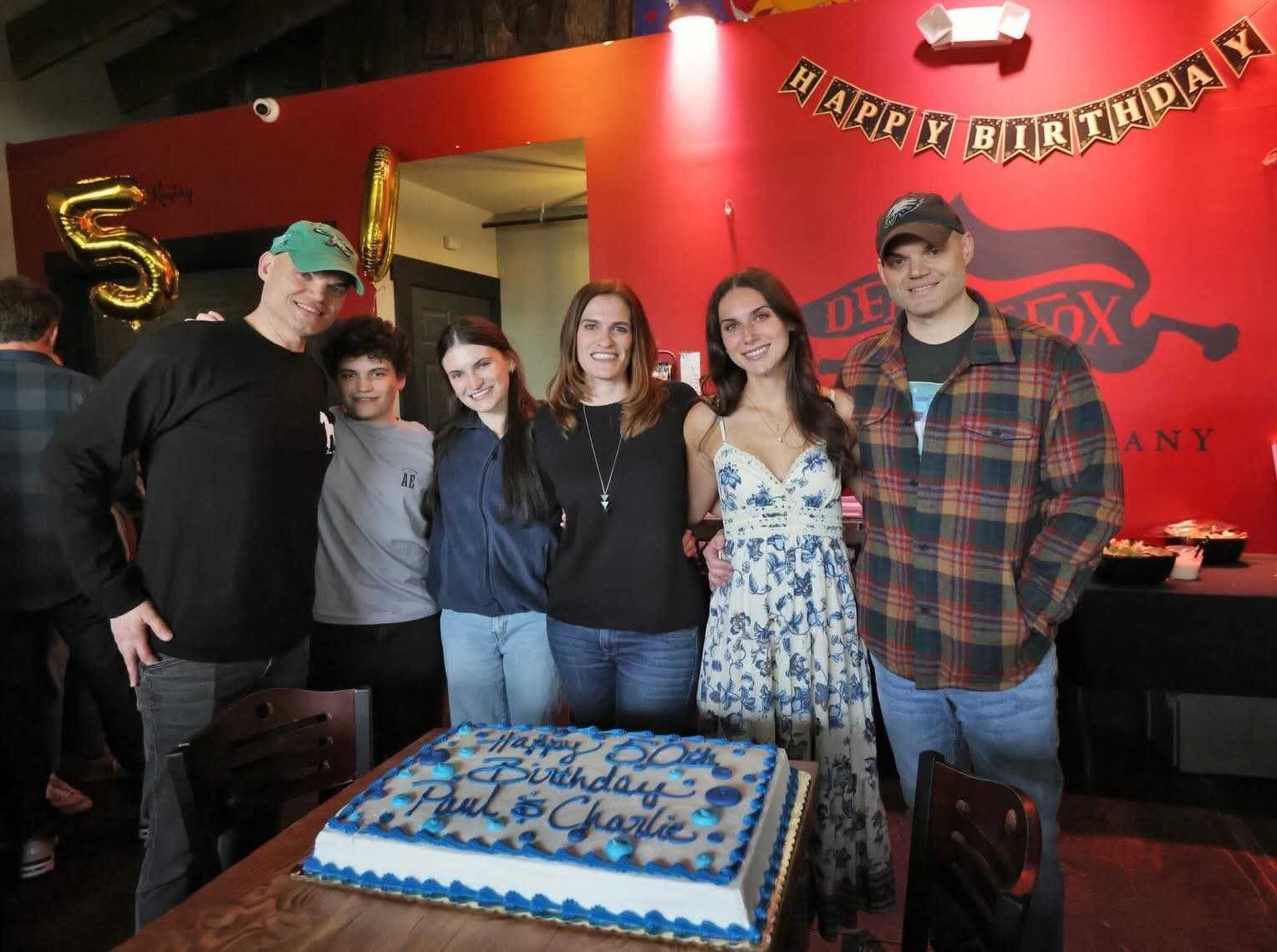 Family gathered around a 50th birthday cake beneath the Death of the Fox mural