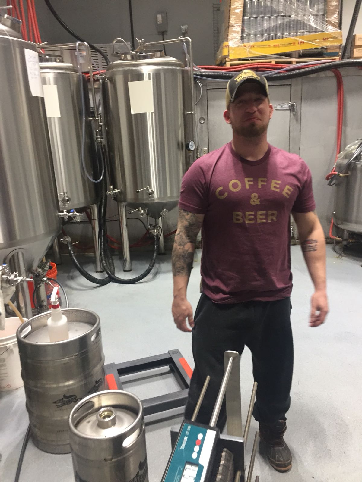 Brewer in a Coffee & Beer shirt among the tanks and kegs at Death of the Fox